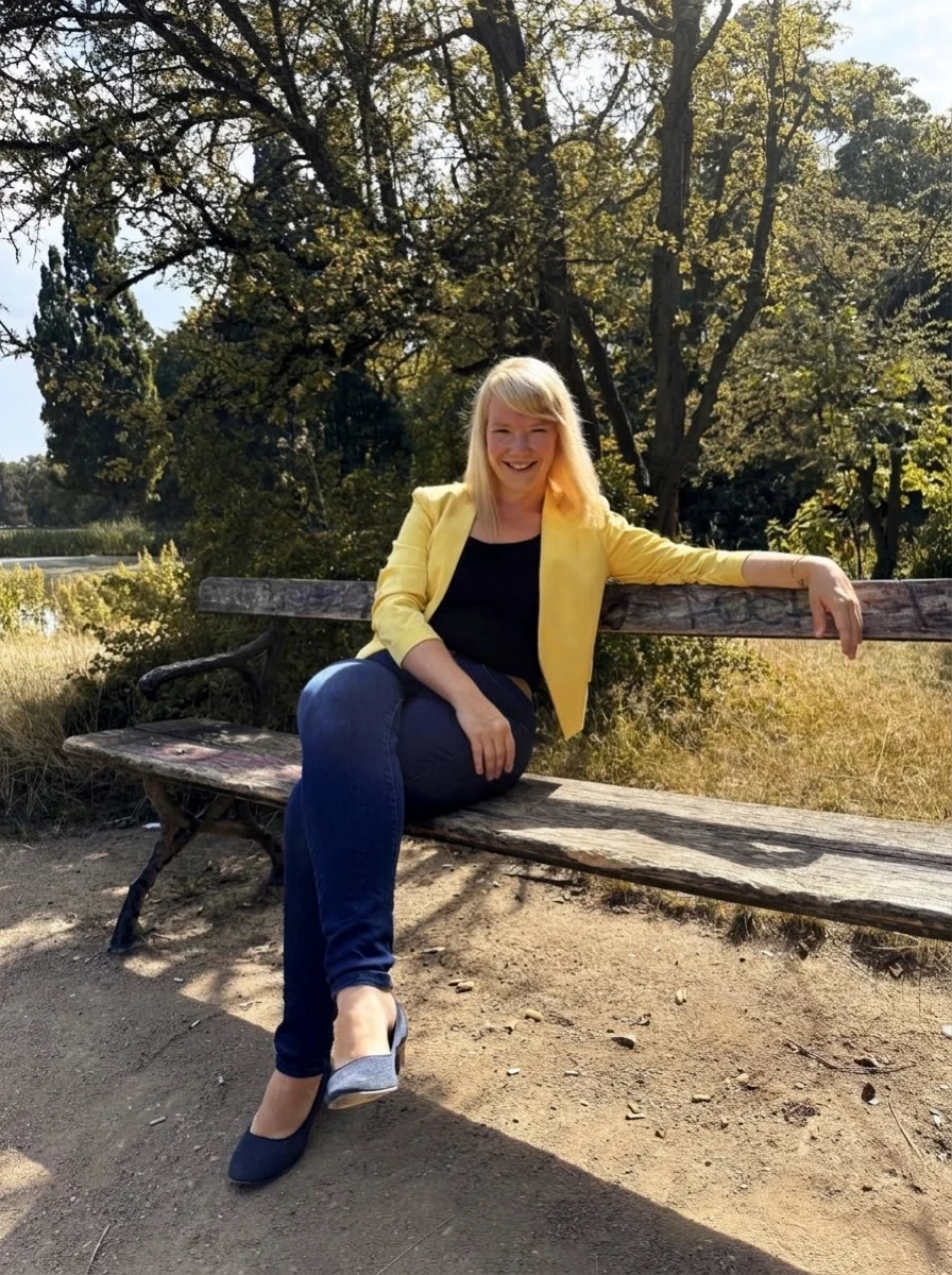 Janine May im gelben Blazer auf einer Parkbank